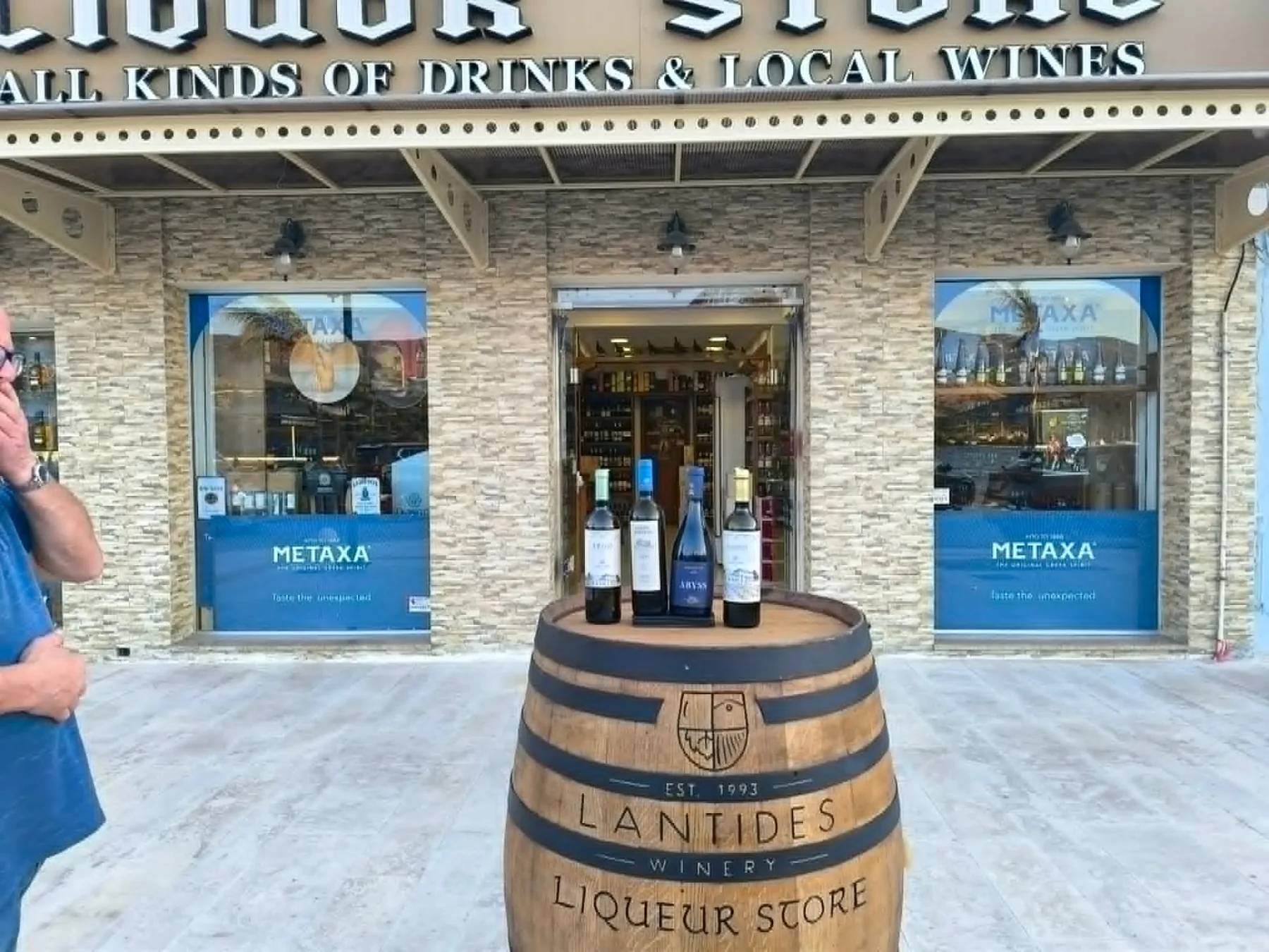 Anagnostatos Liquor Store storefront in Argostoli, Kefalonia — Lantides winery barrel with local Greek wines at the entrance.
